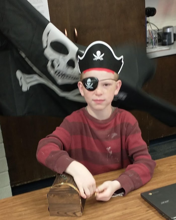 Student dressed as pirate with pirate flag and treasure chest